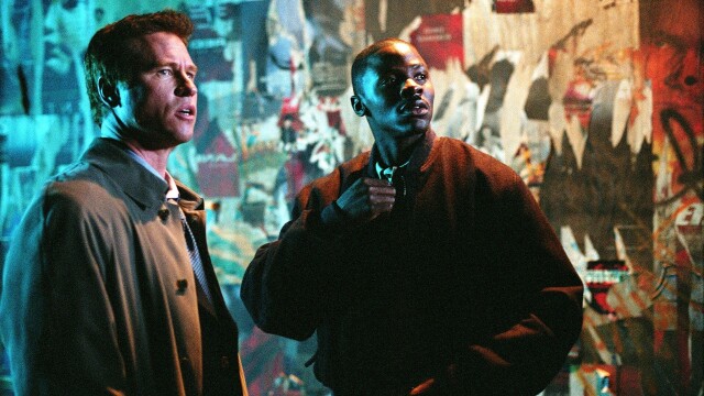 alt="Val Kilmer and Derek Luke standing tensely in front of a graffiti wall in Spartan, 2004 action thriller."
